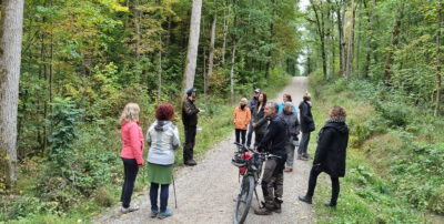 Die Teilnehmerinnen und Teilnehmer der Waldführung stehen auf einem Waldweg und hören den Ausführungen des Försters zu.